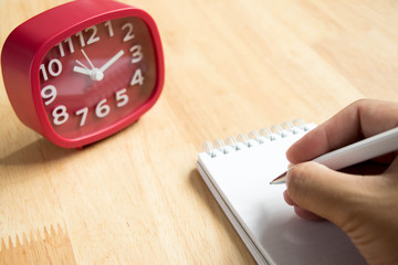 Man hold the pen with book and red clock on wooden table background