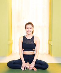 young attractive asian woman in black yoga exercise outfit sitting and smiling at home, bathed warm light from the window