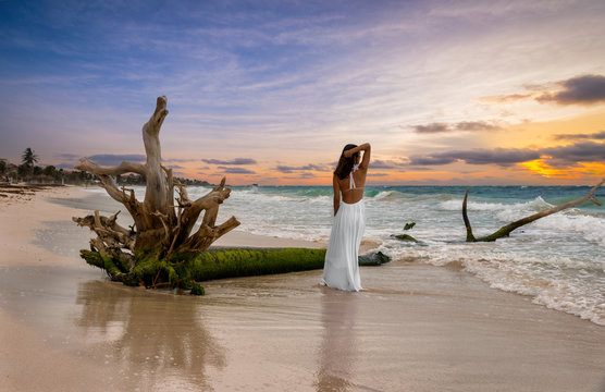 Attraktive Frau im weißen Kleid steht am karibischen Strand während des Sonnenuntergang s