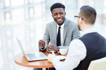 Fototapeta na wymiar Portrait of successful African-American businessman smiling while discussing deal with partner during meeting at coffee break