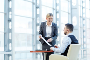 Portrait of smiling young businesswoman presenting documents to client or business partner during meeting