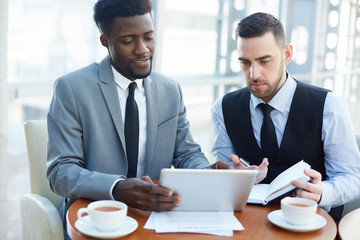 Portrait of successful African-American businessman presenting project on digital tablet to partner...