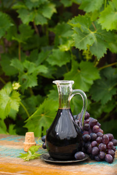 Black old balsamic vinegar in a glass jug with fresh red grapes on green vineyard background