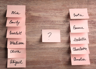 Paper stickers with different names on wooden background. Concept of choosing baby name
