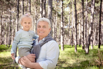 Naklejka na ściany i meble Happy senior man with granddaughter in forest on sunny day