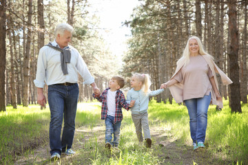 Naklejka na ściany i meble Happy grandparents with little children in forest on sunny day