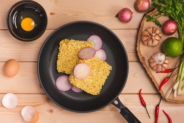 Instant noodles for cooking and eat in the dish with eggs and vegetables on wooden background.
