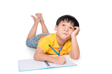 Schoolboy lying on a floor, looking up and writing in notebook.