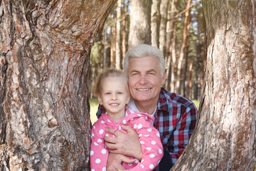 Happy grandfather with little girl near tree on sunny day