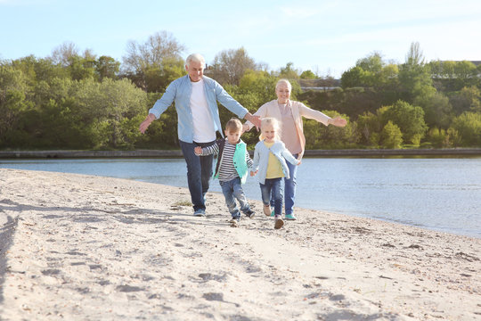 Happy Grandparents Playing With Little Children On River Bank