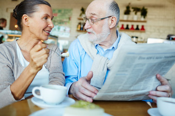 Mature man and woman discussing news from newspaper