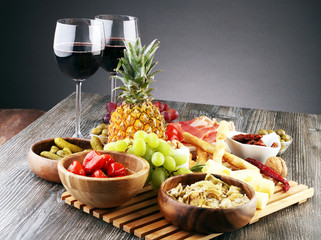 Italian antipasti wine snacks set. Cheese variety, Mediterranean olives, pickles, Prosciutto di Parma with grapes, wine in glasses over black grunge background