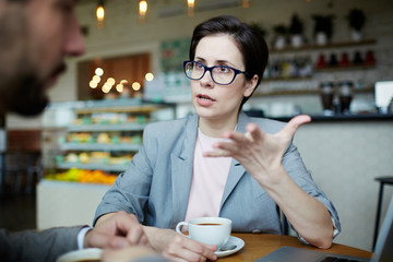 Portrait of confident modern businesswoman meeting with partner in cafe discussing work and gesturing actively