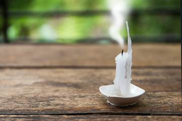 Burning down candle with smoke on wooden table
