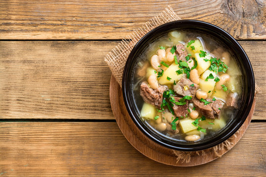 Beef soup with potatoes, beans and leeks in ceramic bowl on stone background.