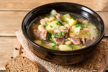 Beef soup with potatoes, beans and leeks in ceramic bowl on stone background.