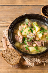 Beef soup with potatoes, beans and leeks in ceramic bowl on stone background.