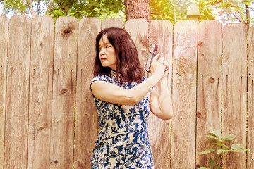 Obraz premium An Asian woman is holding a pistol in front of a wood fence