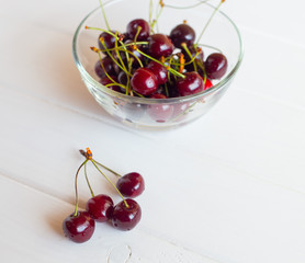 Naklejka na ściany i meble Red cherry in a glass plate on a white background