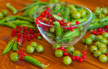 Green peas and red currants on a wooden table.