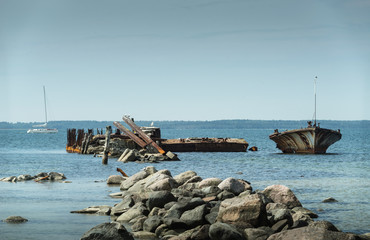 Fototapeta na wymiar Old broken boat wreck on the shore, blue sea and sailboat on background. Harilaid, small island in Estonia, Europe.