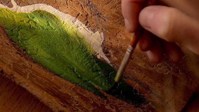 closeup of a female artist painting a green woodpecker on a piece of spruce wood