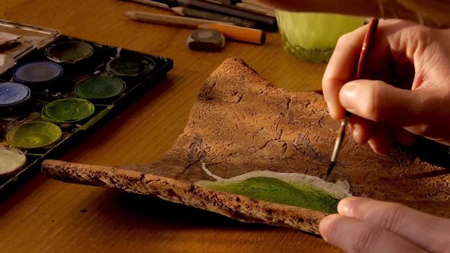 closeup of a female artist painting a green woodpecker on a piece of spruce wood