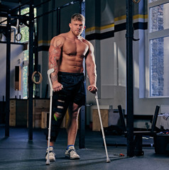 Fototapeta na wymiar Shirtless bodybuilder on crutches near cross fit stand.