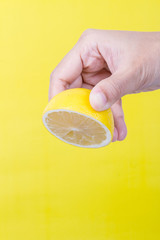 Woman's hand squeezing lemon on yellow background