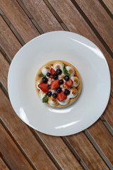 Small tart with buscuit, berries and mint on white plate on wood lath table