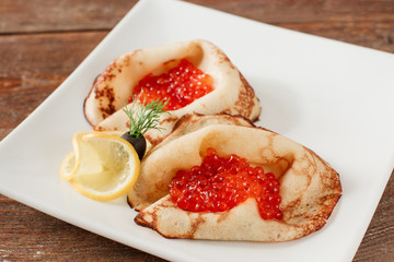 Pancakes with red caviar on white plate. Russian traditional salty crepes with seafood. Shrove tuesday holiday food