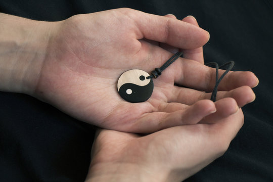 Two Hands Holding Pearl Yin Yang Necklace On Dark Background.