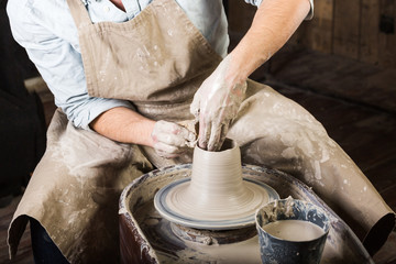 pottery, workshop tools, ceramics art concept - man hands work with potter's wheel, the fingers form the shape of raw fire clay, young male sculpt a utensils with a sponge, master in apron, top view