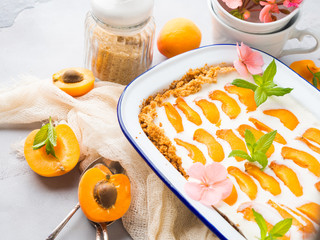 Home made apricot not baked cheese cake in enamel tin on gray background with flowers