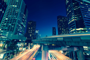 Fototapeta premium Photo of commercial office buildings exterior. Night view at bottom skyscrapers with light of traffic rush, long exposur in Bangkok