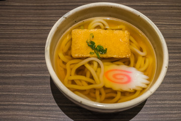 Kitsune Udon Japanese noodles in white bowl on wooden table