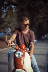 Young attractive man on retro motorbike in park, hipster concept