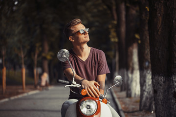 Young attractive man on retro motorbike in park, hipster concept