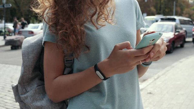 Young brunette woman in a blue t-shirt enjoys a mobile phone in the city, slow motion