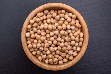 Peeled chickpeas lies in a wooden cup on a stony black board, black background, space for text