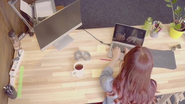 Red haired freelance female working with lap top, talking on the phone. Toned footage view from above on foxe woman at wooden table.