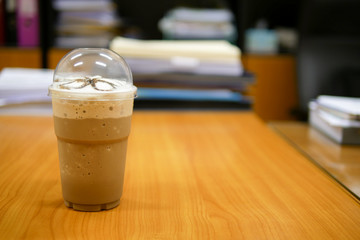 Mocha frappe in a clear plastic glass on a wooden desk in an office, selective focus