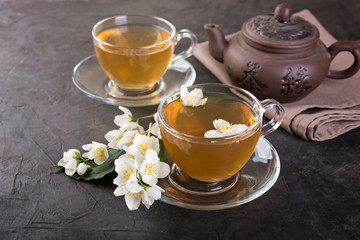 Obraz na płótnie Canvas Glass cups of tea and tea pot with jasmine on a dark background.
