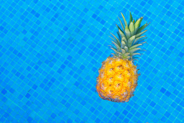 Pineapple floating in water of tiled pool with copy space