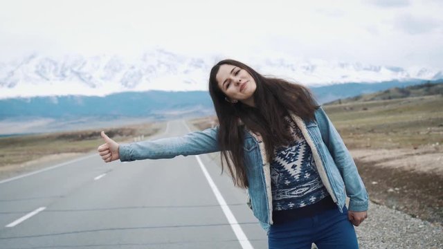 young woman hitch-hiking on a road at the fields. Young girl hippy hitchhiking on the road. Among the mountains in nature. Going on the road