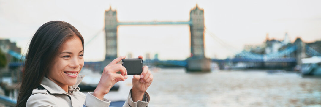 London woman tourist taking photo of Tower Bridge banner panorama. London woman taking photos with mobile smart phone camera. Girl at River Thames, London, England, Great Britain. UK tourism.