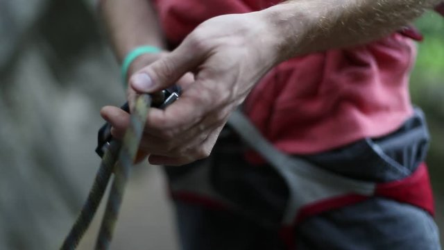 Rock climbing detail of climber harness. Man locking carabiner and catching the rope with rustic hands about to belay. Slow motion 120 fps detail close up scene. Risk outdoor sport. Patagonia.