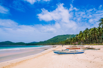 Local boats on wide Nacpan Beach on sunny day. El Nido, Palawan, Philippines