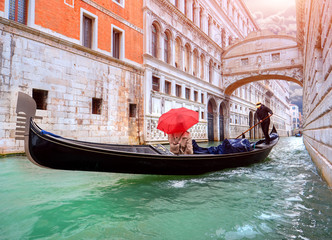 Obraz na płótnie Canvas Woman with a red umbrella in Gondola passing over Bridge of Sighs in Venice