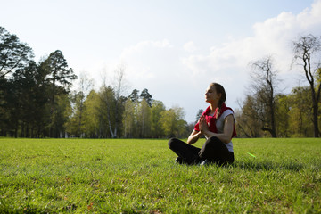 Naklejka na ściany i meble Meditating yoga young woman on grass, lotus, exercise, park, forest, space, trees, outdoor, natural background